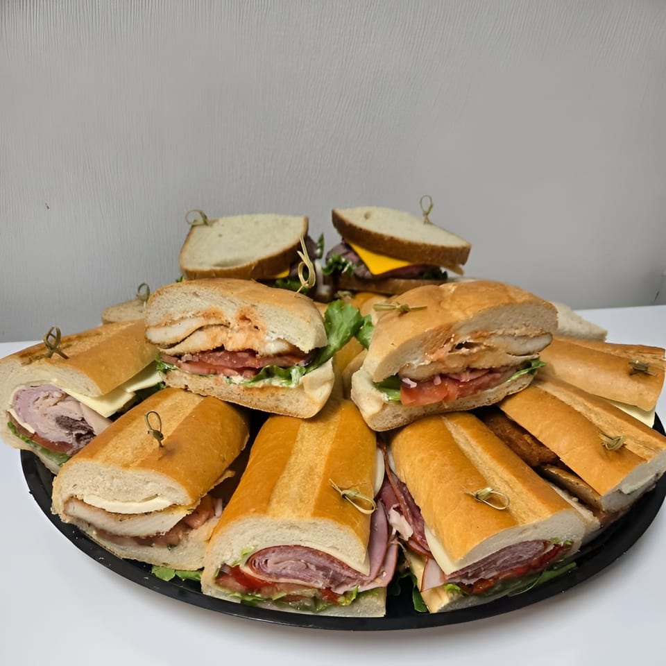 A catering platter from Trento Gourmet Deli with various sandwiches and subs, some cut in half.