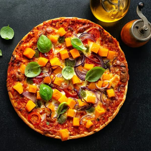 Trento Gourmet Deli Catering pizza with butternut squash, red onion, and basil on a dark surface.