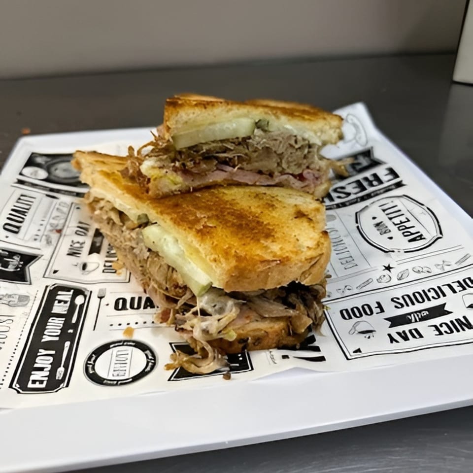 A grilled deli sandwich, cut in half, filled with pulled meat and melted cheese on a white plate.