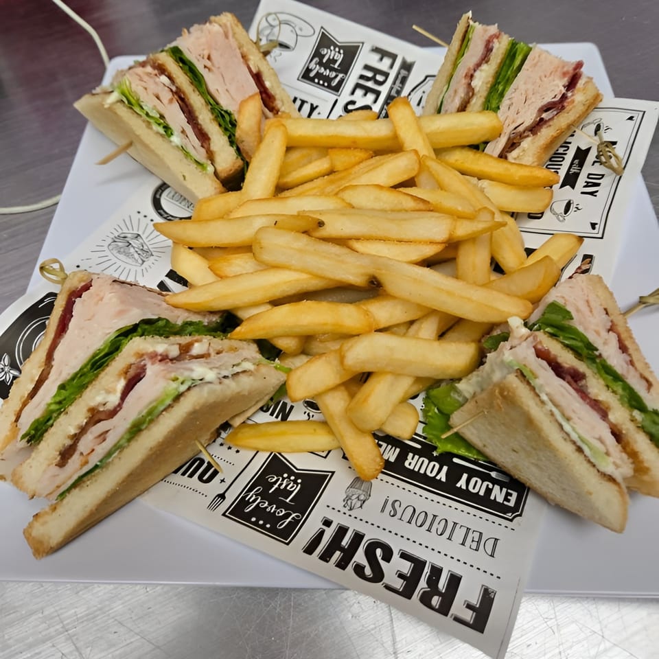 Four club sandwiches with turkey, bacon, and lettuce, served with a pile of golden french fries.